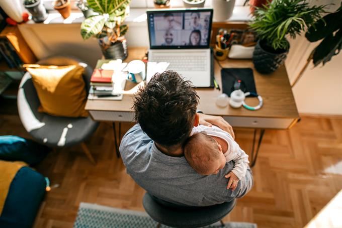 Photo of a man working from home, with his newborn baby as a company, having a video conference call