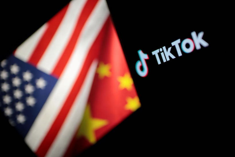 TikTok logo is seen on a mobile phone screen in front of US and Chinese flags