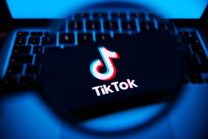 Magnifying glass held over smart phone displaying TikTok logo
