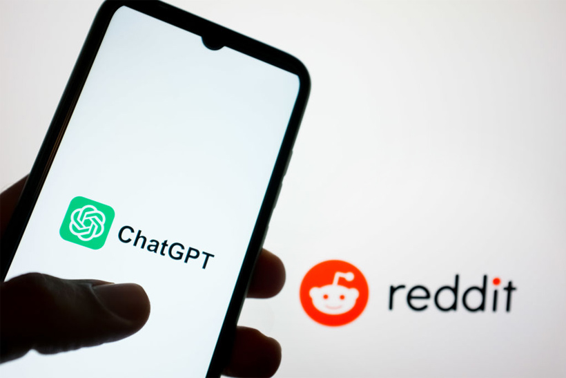 Hand holding smart phone displaying ChatGPT logo next to Reddit logo